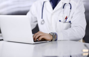 Bilinmeyen bir erkek doktor klinikte dizüstü bilgisayarla yakın planda çalışıyor. İşteki genç doktor. Mükemmel sağlık hizmeti, tıp konsepti