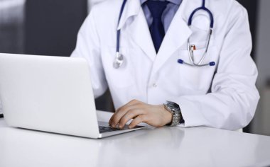 Bilinmeyen bir erkek doktor klinikte dizüstü bilgisayarla yakın planda çalışıyor. İşteki genç doktor. Mükemmel sağlık hizmeti, tıp konsepti