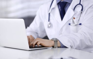 Bilinmeyen bir erkek doktor klinikte dizüstü bilgisayarla yakın planda çalışıyor. İşteki genç doktor. Mükemmel sağlık hizmeti, tıp konsepti