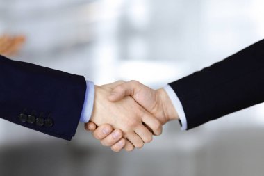 İş adamları toplantıda ya da pazarlıkta el sıkışıyor, yakın plan. Bir grup tanınmamış iş adamı ve modern bir ofiste duran bir kadın. Takım çalışması, ortaklık ve el sıkışma kavramı