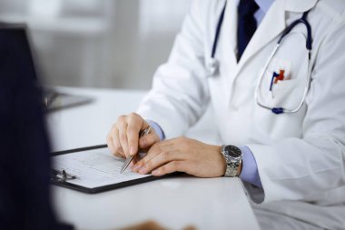 Bir doktor, hastanedeki dolapta birlikte otururken hastasıyla konuşuyor. Doktor ilaç kayıtlarını doldurmak için pano kullanıyor. Mükemmel tıbbi hizmet...