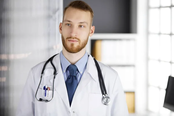 Der rotbärtige Arzt steht direkt in der Klinik in der Nähe seines Arbeitsplatzes. Porträt eines Arztes. Medizin und Gesundheitskonzept — Stockfoto