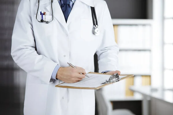 Neznámý mužský lékař stojí a píše se záznamníkem na klinice na svém pracovišti. Koncept medicíny — Stock fotografie