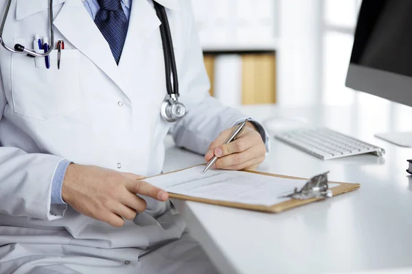 Amistoso médico de barba roja sentado y escribiendo con portapapeles en la clínica, de cerca. Concepto de medicina — Foto de Stock