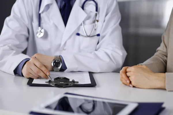 Médico desconhecido e mulher paciente discutindo algo enquanto estava sentado na clínica e usando prancheta. Melhor serviço médico no hospital, medicina, parada pandêmica — Fotografia de Stock