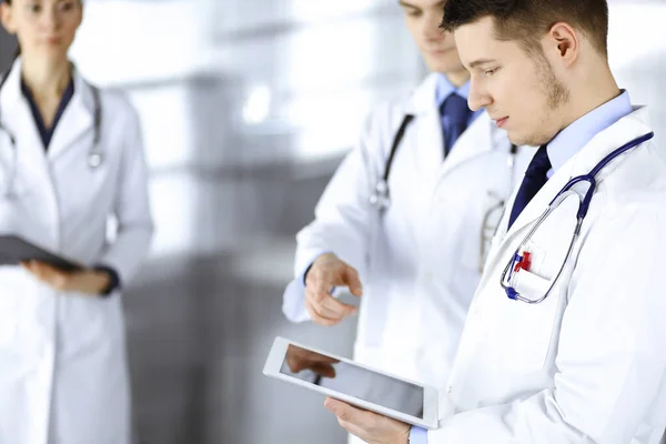Een groep artsen controleert medische namen op een tablet, met een verpleegkundige met een klembord op de achtergrond, die samen in een ziekenhuiskantoor staat. Artsen klaar om patiënten te onderzoeken en te helpen — Stockfoto