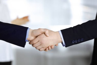İş adamları toplantıda ya da pazarlıkta el sıkışıyor, yakın plan. Bir grup tanınmamış iş adamı ve modern bir ofiste duran bir kadın. Takım çalışması, ortaklık ve el sıkışma kavramı