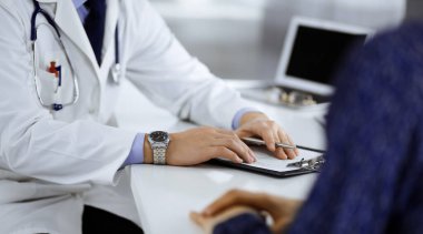 Bir doktor, hastanedeki dolapta birlikte otururken hastasıyla konuşuyor. Doktor ilaç kayıtlarını doldurmak için pano kullanıyor. Mükemmel tıbbi hizmet...