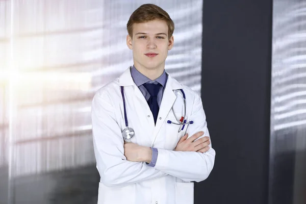 Genç doktor, iş yerinin yakınındaki güneşli klinikte çapraz kollarla duruyor. Tıp konsepti — Stok fotoğraf