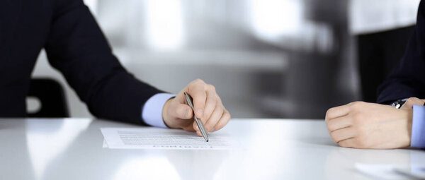Business people discussing a contract at meeting or negotiation, sitting at the desk together, and an unknown woman on the background, close-up. Group of unknown businessmen in a modern office