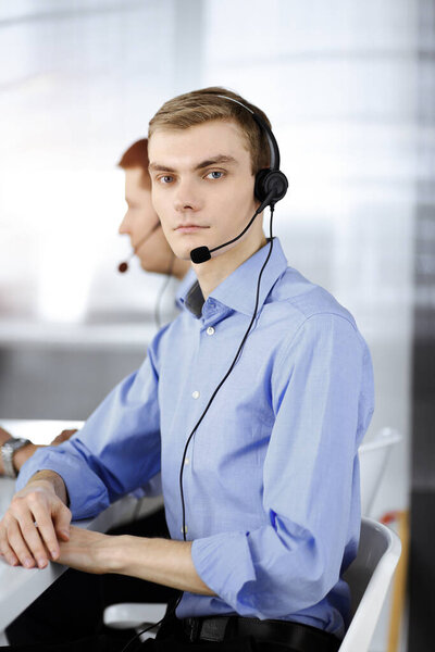 Two young men in headset, sitting at the desk in a sunny modern office, listening to the clients. Call center operators at work