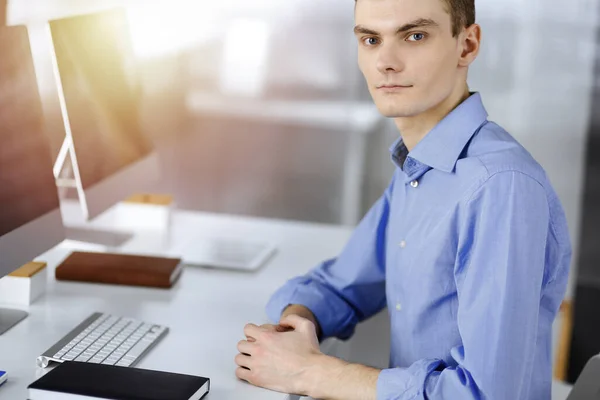 Jeune homme d'affaires prospère travaille avec l'ordinateur, assis au bureau dans un bureau moderne ensoleillé. Prise de vue de l'entrepreneur masculin ou it-spécialiste sur le lieu de travail. Concept d'entreprise — Photo
