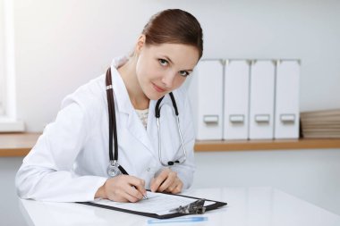 Kadın doktor güneşli klinikte oturuyor ve çalışıyor. Kadın doktor portresi