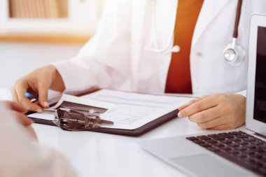 Bilinmeyen bir kadın-doktor hastaya danışmanlık yapıyor ve güneşli odada ilaç geçmişi olan bir dosya kullanıyor. Tıp konsepti