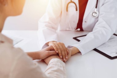 Kimliği belirsiz kadın doktorun elleri güneşli odada kadın hastasına güvence veriyor.
