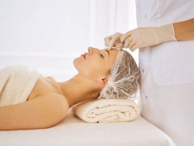 Güzel bir kadın kapalı gözlerle güzellik iğneleri yaptırıyor. Güzellik uzmanı elleri şırıngayla kadın yüzüne güzellik prosedürü uyguluyor.