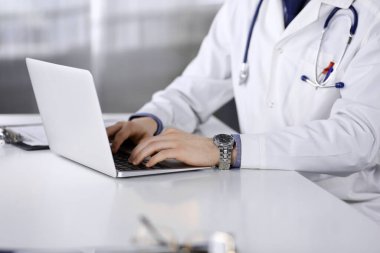 Bilinmeyen bir erkek doktor klinikte dizüstü bilgisayarla yakın planda çalışıyor. İşteki genç doktor. Mükemmel sağlık hizmeti, tıp konsepti