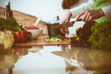 Mutfakta pişen bilinmeyen insan elleri. Yeşil soğan dilimleyen bir kadın. Sağlıklı yemek ve vejetaryen gıda konsepti.