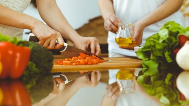Mutfakta yemek pişiren insan ellerine yakın çekim. Anne kız ya da iki kız arkadaş taze salata için sebze kesiyor. Arkadaşlık, aile yemeği ve yaşam tarzı kavramları.