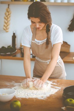 Genç esmer kadın mutfakta pizza ya da el yapımı makarna pişiriyor. Ev hanımı ahşap masada hamur hazırlıyor. Diyet, gıda ve sağlık konsepti