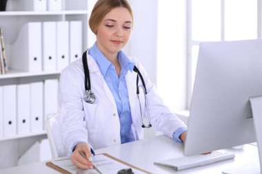Hastanedeki genç bayan doktor masaüstü bilgisayar monitörüne bakıyor. Doktor ilaç geçmişi ve sınav sonuçlarını kontrol ediyor. Tıp ve sağlık hizmetleri kavramı