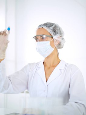 Koruyucu gözlüklü profesyonel kadın bilim adamı laboratuarda reaktörlerle araştırma tüpü kullanıyor. Tıp ve araştırma kavramları