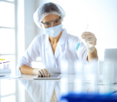 Koruyucu gözlüklü profesyonel kadın bilim adamı laboratuarda reaktörlerle araştırma tüpü kullanıyor. Tıp ve araştırma kavramları