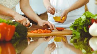 Mutfakta yemek pişiren insan ellerine yakın çekim. Anne kız ya da iki kız arkadaş taze salata için sebze kesiyor. Arkadaşlık, aile yemeği ve yaşam tarzı kavramları.