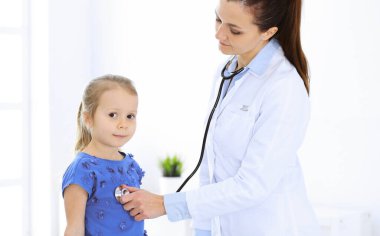 Doktor steteskopla küçük bir kızı muayene ediyor. Her zamanki tıbbi muayenede gülümseyen çocuk hasta. Tıp ve sağlık hizmetleri kavramları