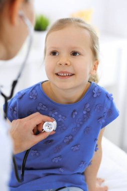 Doktor steteskopla küçük bir kızı muayene ediyor. Her zamanki tıbbi muayenede gülümseyen çocuk hasta. Tıp ve sağlık hizmetleri kavramları