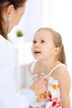 Doktor steteskopla küçük bir kızı muayene ediyor. Her zamanki tıbbi muayenede gülümseyen çocuk hasta. Tıp ve sağlık hizmetleri kavramları