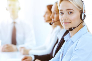 Güneşli ofiste çalışan bir grup farklı telefon operatörü. Kulaklıklı yakışıklı iş kadını müşterilere danışıyor. Çağrı merkezi ve iş adamları kavramı