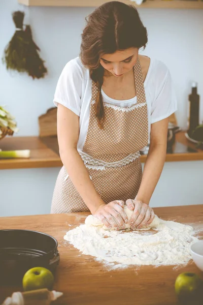 Mladá brunetka žena vařící pizzu nebo ručně dělané těstoviny v kuchyni. Hospodyně připravuje těsto na dřevěném stole. Dietní, stravovací a zdravotní koncepce — Stock fotografie