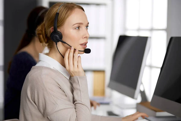 Femme d'affaires amicale parlant par casque dans le bureau. Centre d'appels et divers groupes de personnes en affaires — Photo