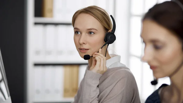 Femme d'affaires amicale parlant par casque dans le bureau. Centre d'appels et divers groupes de personnes en affaires — Photo