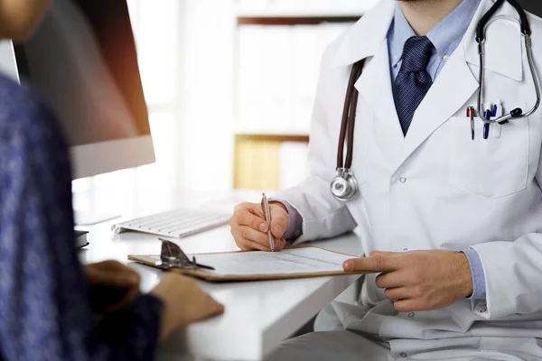 Amigável médico de barba vermelha e mulher paciente discutindo o exame de saúde atual enquanto sentado na clínica ensolarada. Conceito de medicina — Fotografia de Stock