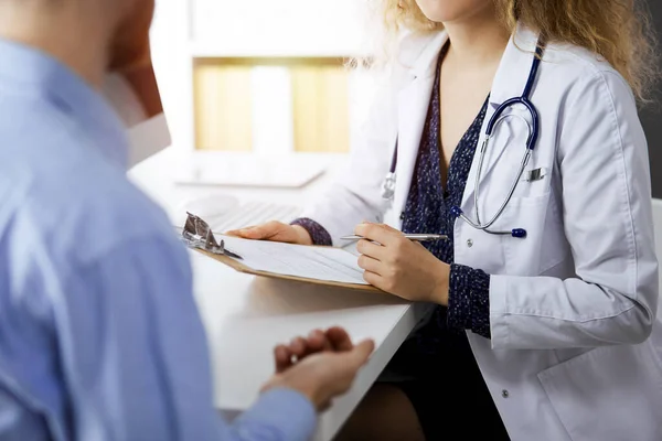 Médico femenino y paciente masculino discutiendo el examen de salud actual mientras está sentado en una clínica soleada, de cerca. Concepto de medicina — Foto de Stock