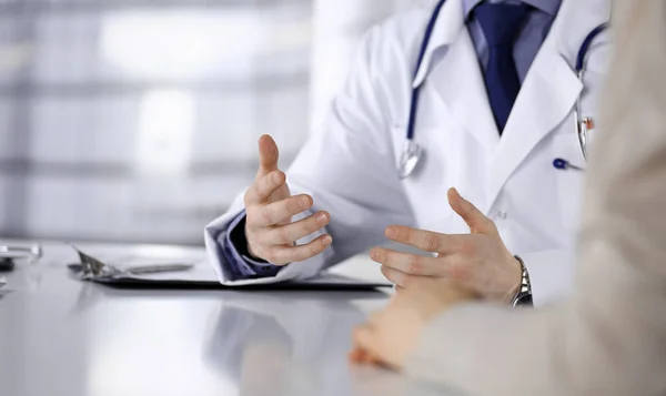 Unknown male doctor and patient woman discussing something while sitting in clinic and using clipboard. Best medical service in hospital, medicine, pandemic stop — Stock Photo, Image