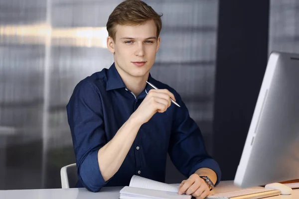 Jeune homme d'affaires blond réfléchissant à la stratégie à son lieu de travail avec ordinateur. Démarrage d'entreprise signifie travailler dur et hors du temps pour la réussite — Photo