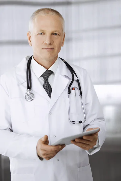 Idosos médico confiante em pé em linha reta e usando tablet na clínica. Serviço médico perfeito. Conceito de medicina e saúde — Fotografia de Stock