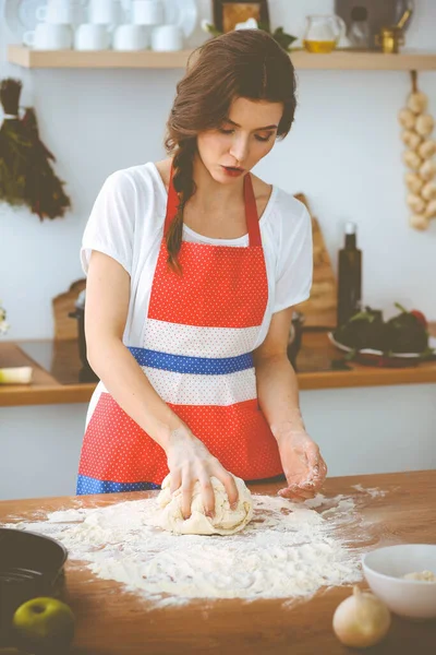 Jovem morena cozinhando pizza ou massa artesanal na cozinha. Dona de casa que prepara a massa de farinha na mesa de madeira. Conceito de alimentação, alimentação e saúde — Fotografia de Stock