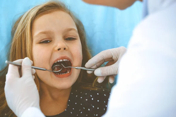 Liten flicka sitter vid tandstolen med öppen mun under oral kontroll medan läkare. Besökande tandläkarmottagning. Medicinskt koncept. Tonat foto — Stockfoto