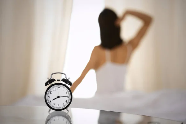 Femme étirant les mains au lit après le réveil, éruption de soleil. Brunette entrant dans une journée heureuse et détendue après une bonne nuit de sommeil et vue arrière. Concept d'une nouvelle journée et d'un week-end joyeux — Photo