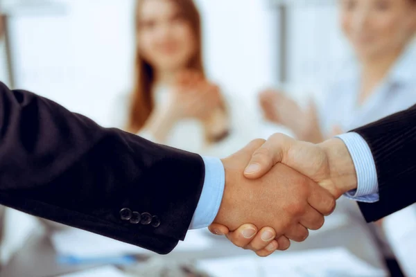 Business people shaking hands at meeting while theirs colleagues clapping and applauding. Group of unknown businessmen and women in modern white office. Success teamwork, partnership and handshake — Stock Photo, Image