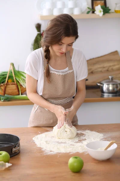 Jonge brunette vrouw koken pizza of handgemaakte pasta in de keuken. Huisvrouw maakt deeg op houten tafel. Dieet-, voedings- en gezondheidsconcept — Stockfoto