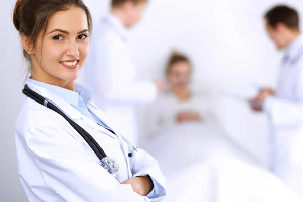 Female doctor smiling on the background with patient in the bed and two doctors