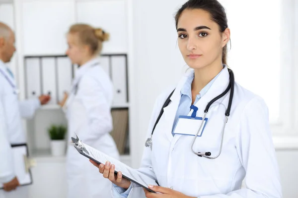 Dottoressa in clinica con colleghi sullo sfondo. Personale ispanico o latino americano in medicina — Foto Stock