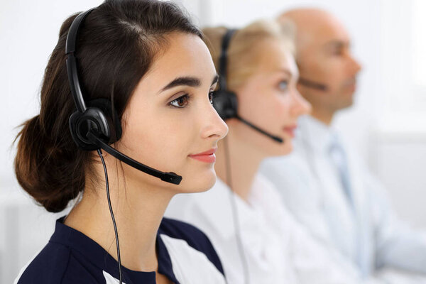 Call center operators at work. Focus at beautiful latin american woman in headset