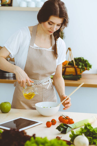 Молодая брюнетка готовит на кухне. Домохозяйка держит в руке деревянную ложку. Концепция питания и здоровья