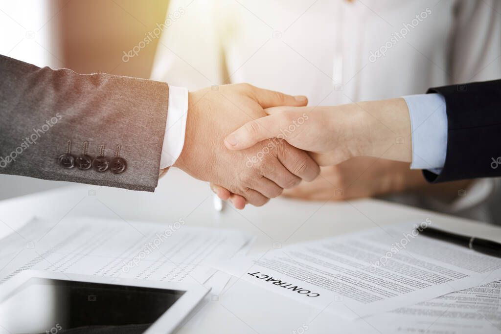 Business people shaking hands finishing contract signing in sunny office, close-up. Handshake and marketing